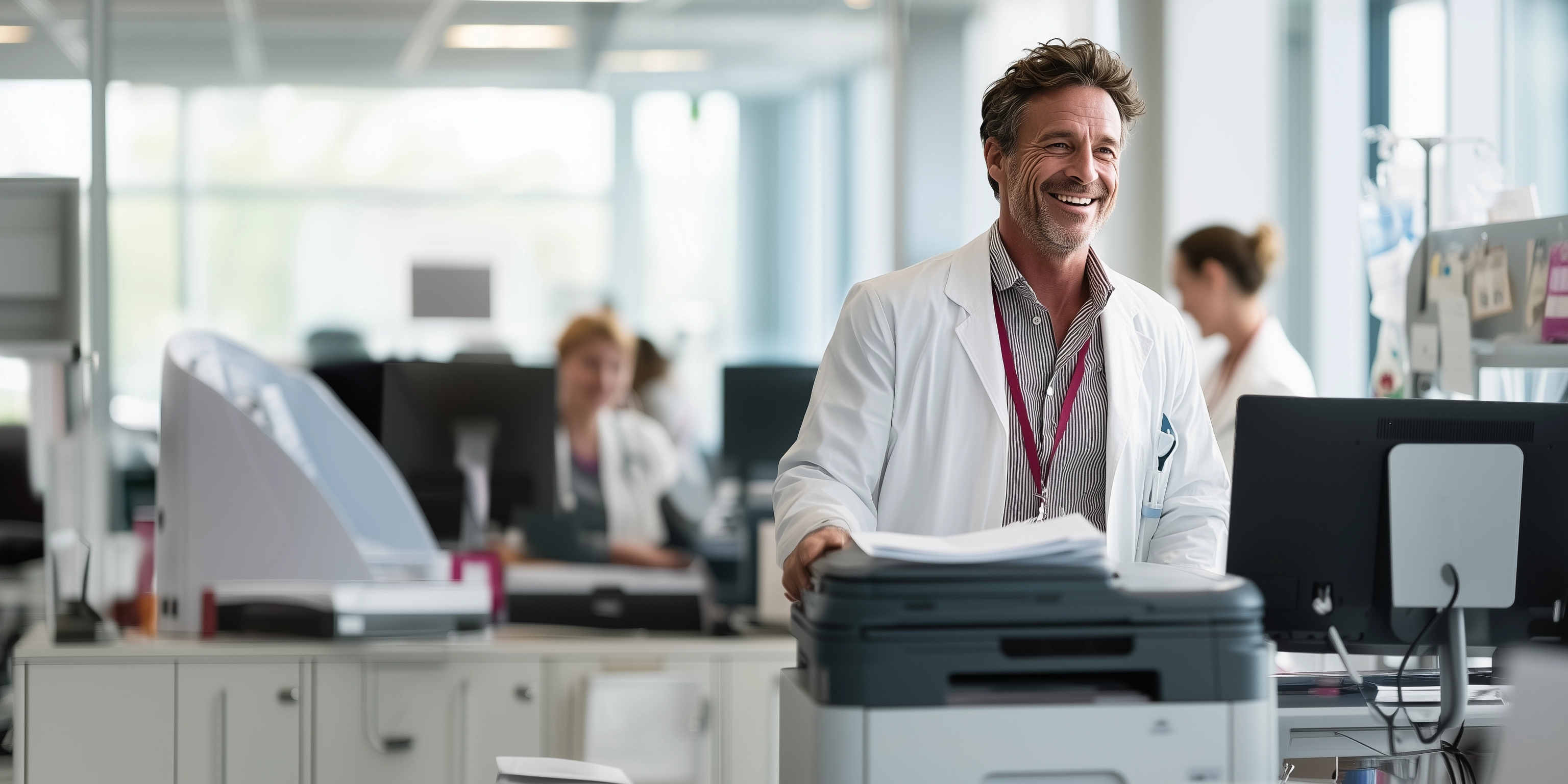 A smiling clinician in a white coat collects documents at an office multifunction printer.